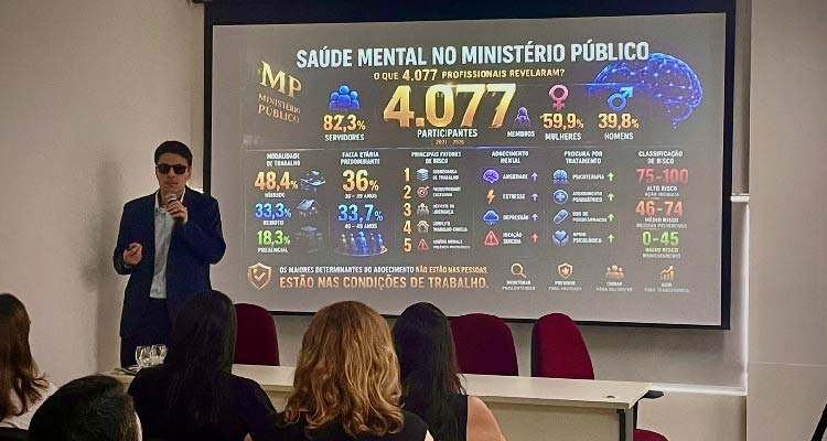 Imagem do palestrante falando diante do público com imagens de slides projetadas atrás dele