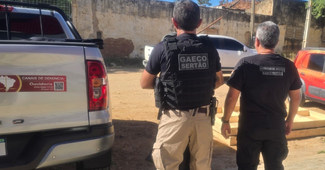 Foto mostra dois integrantes do Gaeco de costas, vestindo coletes pretos com a inscrição Gaeco Sertão